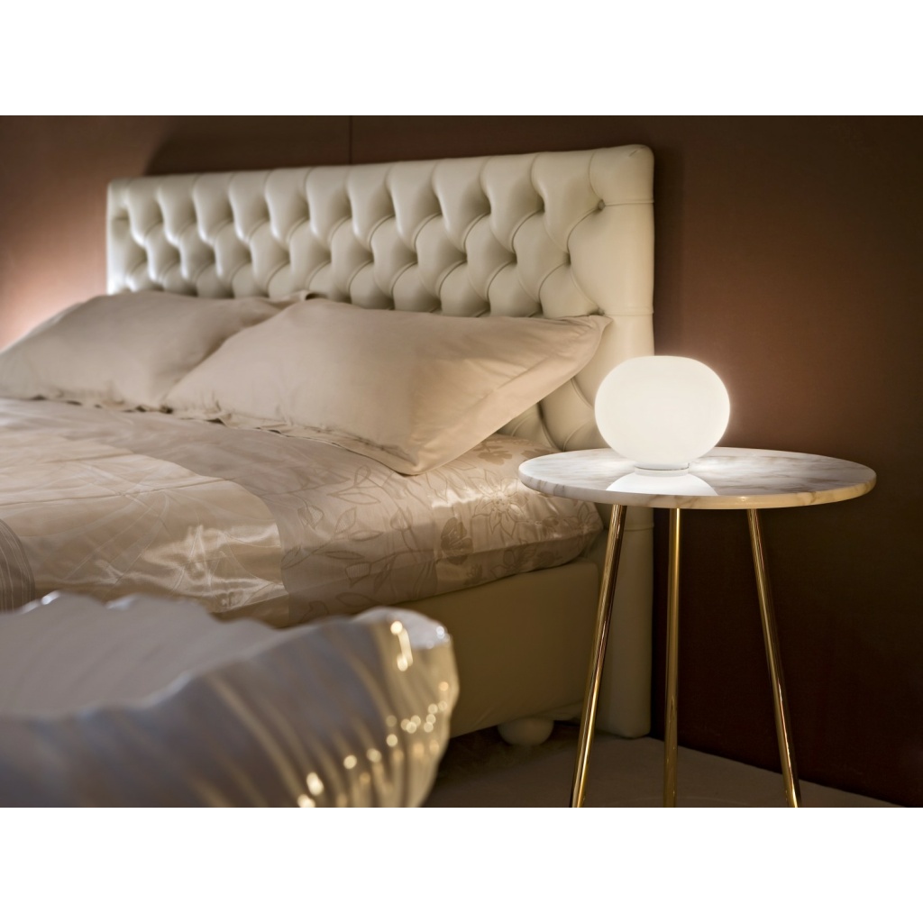 Glo-Ball bordlampe fra FLOS gir mykt, varmt lys på nattbordet i et soverom med lyse tekstiler